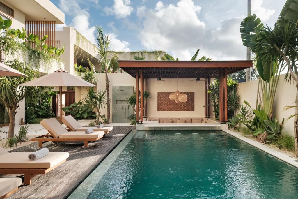 an outdoor pool with chaise lounge chairs and a house at Manu Villas in Sanur