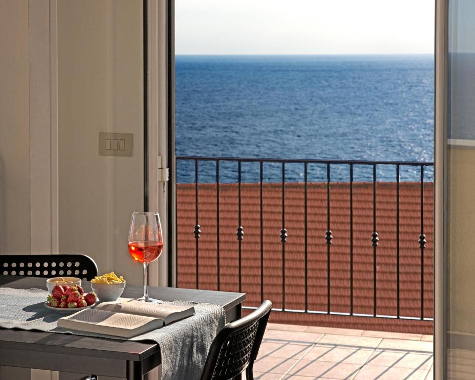 a table with a glass of wine and a view of the ocean at Parasio - Mareri apartments in Imperia