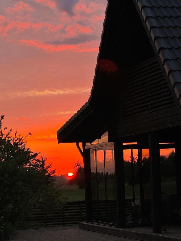 a sunset behind a building with the sun in the background at Pakarklių sodyba in Anykščiai