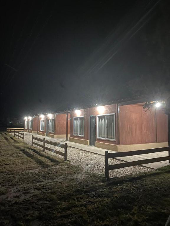 a building with a fence in a field at night at Cabañas Emilia in La Adela