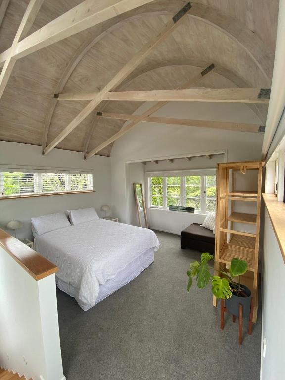 a bedroom with a large white bed and windows at Kauri Coast Bungalow in Karekare