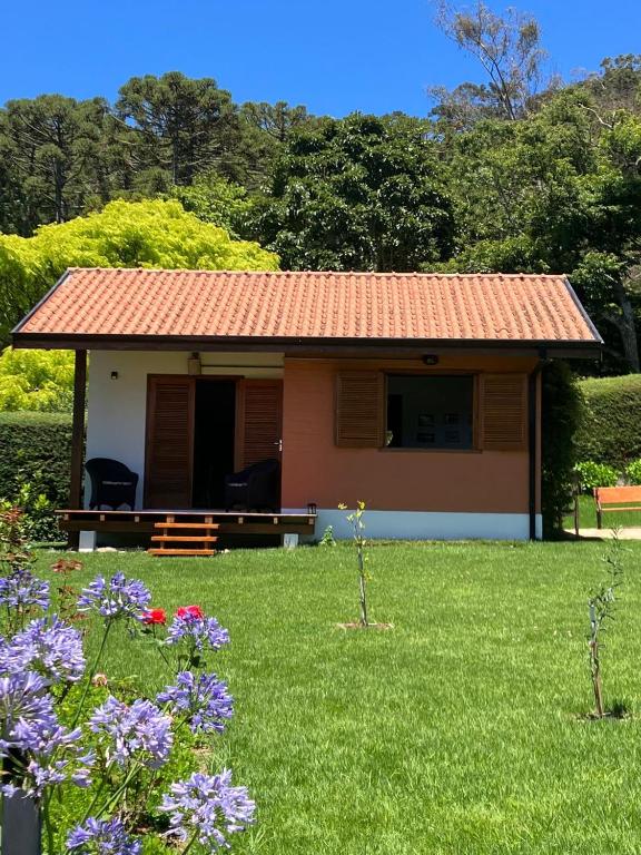 a small house with a green yard with flowers at Chalé das Flores - Refúgio com clima de chácara no Centro de Gonçalves in Gonçalves