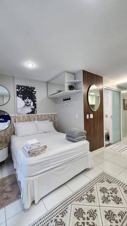 a bedroom with a large white bed and a mirror at Studio Costa a Mar in Guarapari