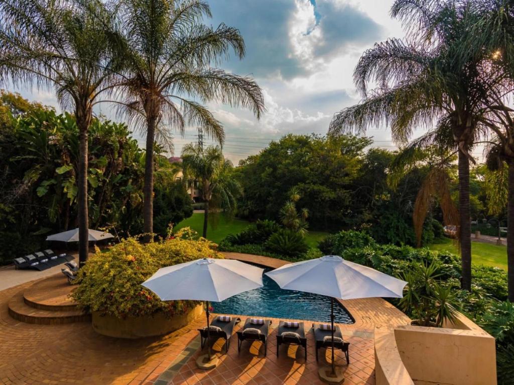 a pool with two umbrellas and chairs and palm trees at Hagios House in Pretoria