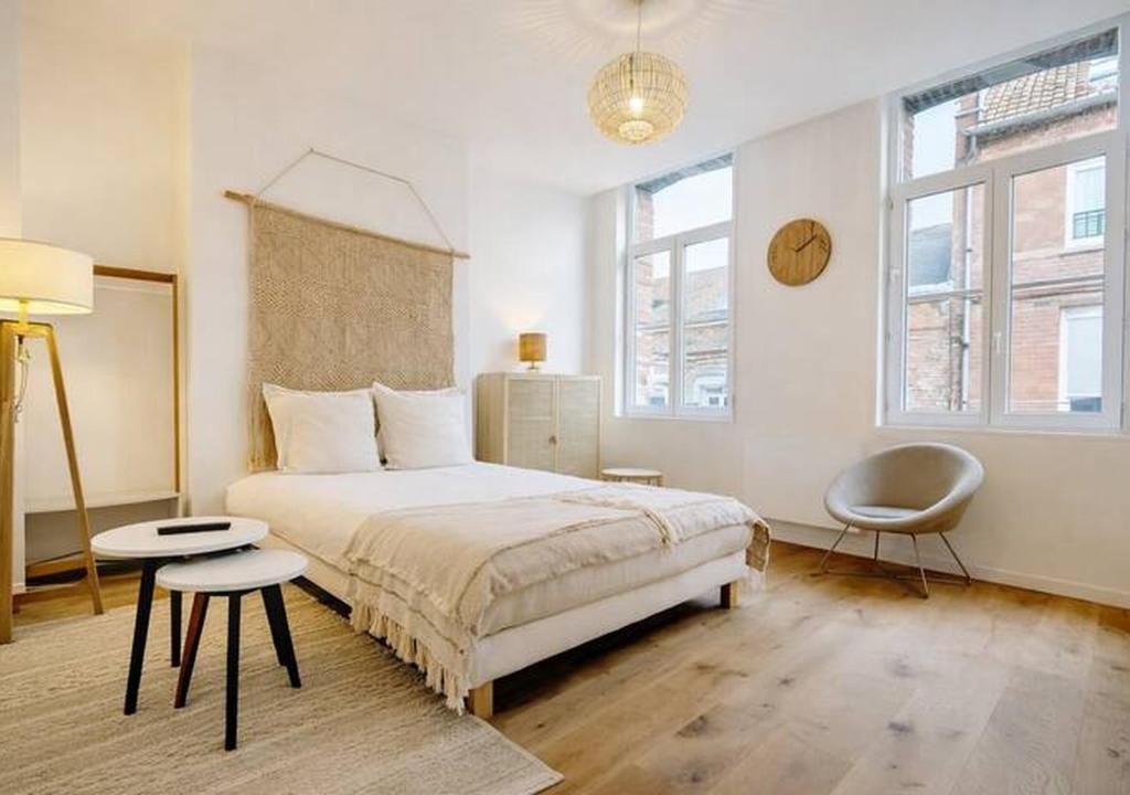a bedroom with a bed and a chair and two windows at Spacious & Luxuary Studio in Amiens