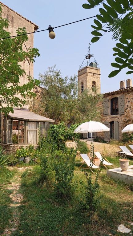 a building with an umbrella and chairs and a church at La Potentille in Lieuran-Cabrières