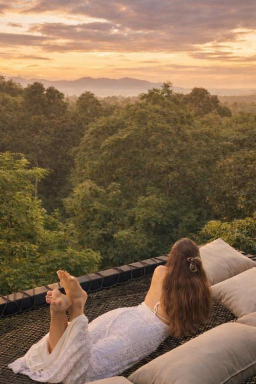 a woman laying on a bed looking out at the forest at Exclusive Luxury 3-Bedroom Jungle Villa with Private Infinity Pool, Breathtaking Sea View & Peaceful Nature Escape in Mae Nam