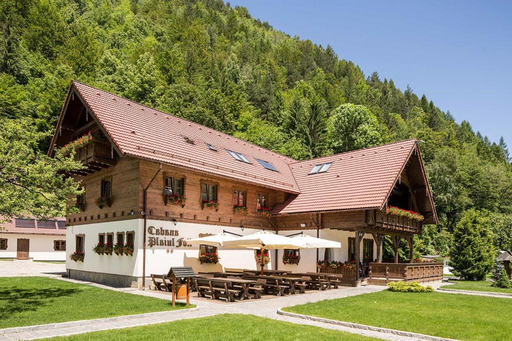 a building with tables and umbrellas in front of a mountain at Cabana Plaiul Foii in Zărneşti