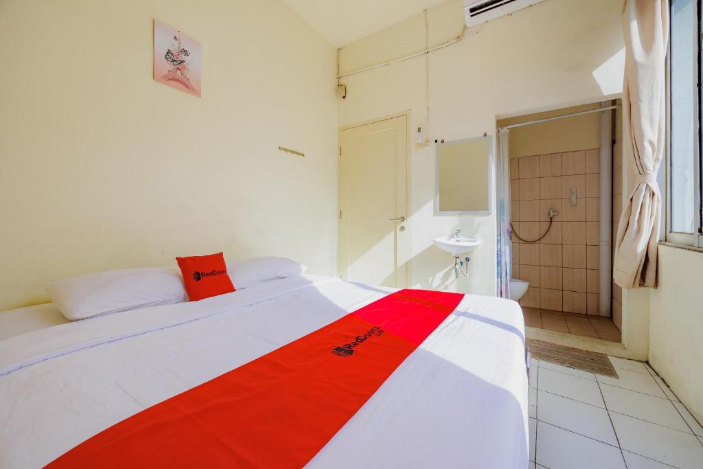a bedroom with a red and white bed and a bathroom at RedDoorz near Soekarno Hatta Airport 3 in Tangerang