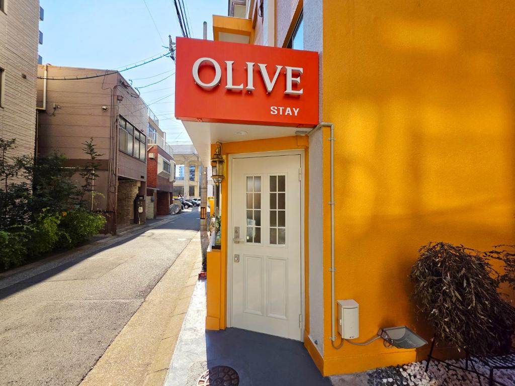 a sign on the side of a yellow building with a white door at OLIVE Stay in Fukuoka