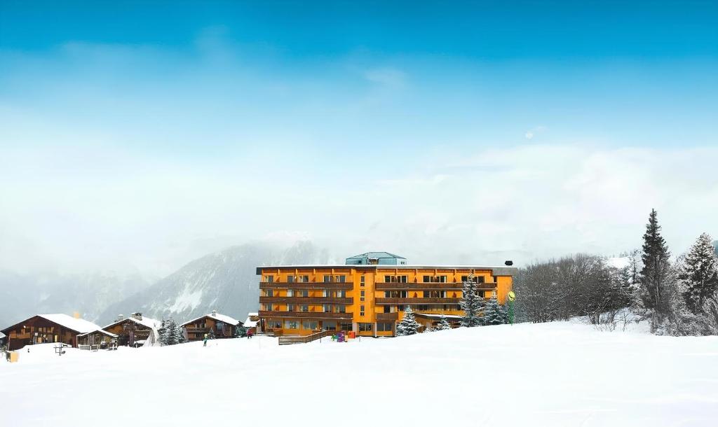 a yellow building in the snow with a mountain at Crystal Hôtel in Courchevel