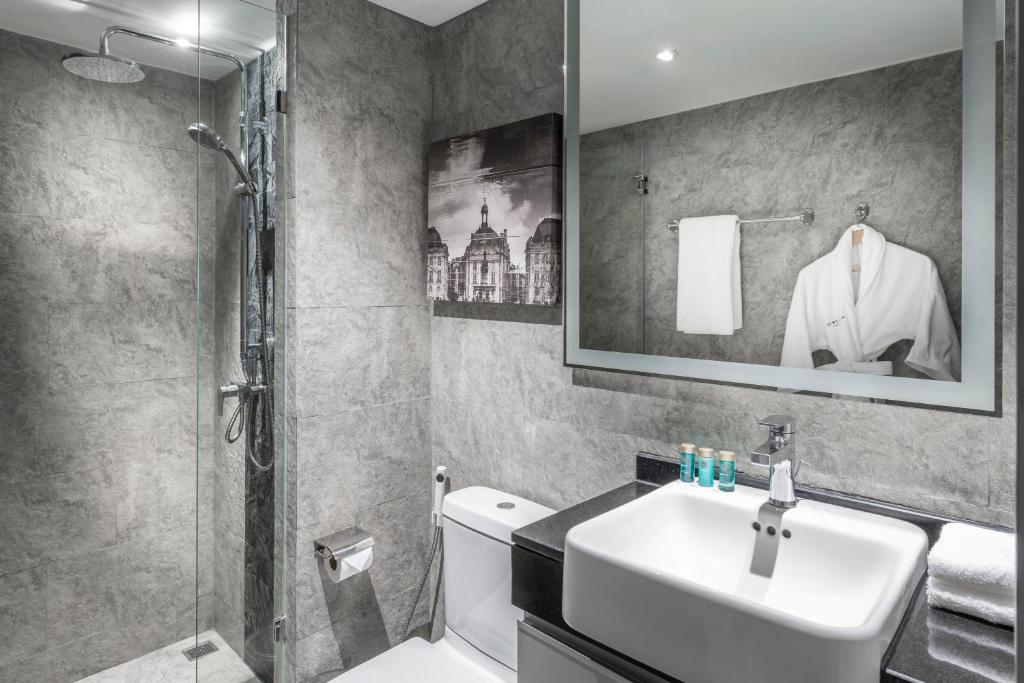 A compact gray-tiled bathroom with a glass shower, wall-mounted rain shower and vanity.