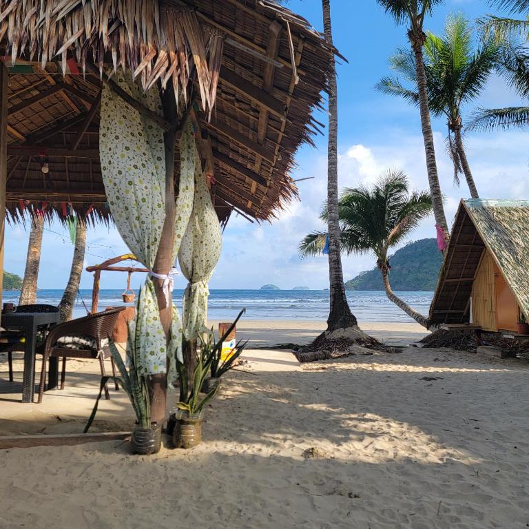a beach with a straw umbrella and palm trees at Island Crib in El Nido