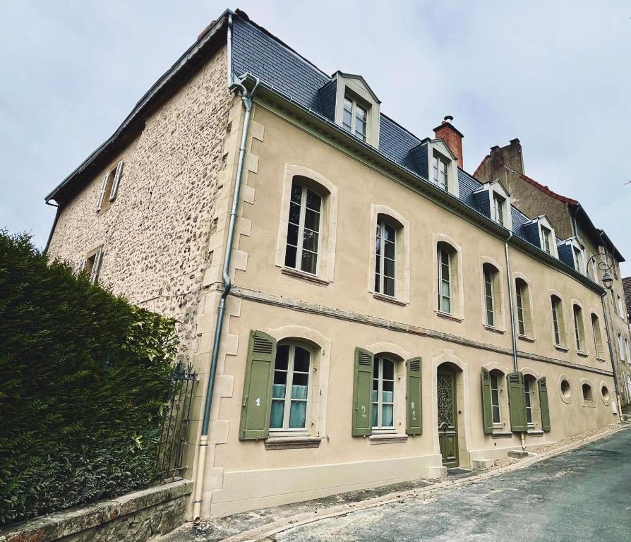 a large white building with green shutters on a street at Les Glycines 23300 in La Souterraine