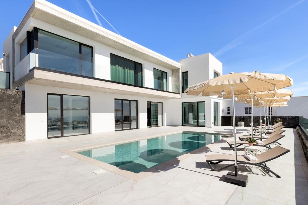 a house with a swimming pool with chairs and umbrellas at Ocean View Lanzarote by Beyond in Tías