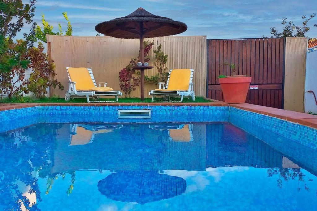 a swimming pool with two chairs and an umbrella at Vila Saraz Alqueva in Campinho