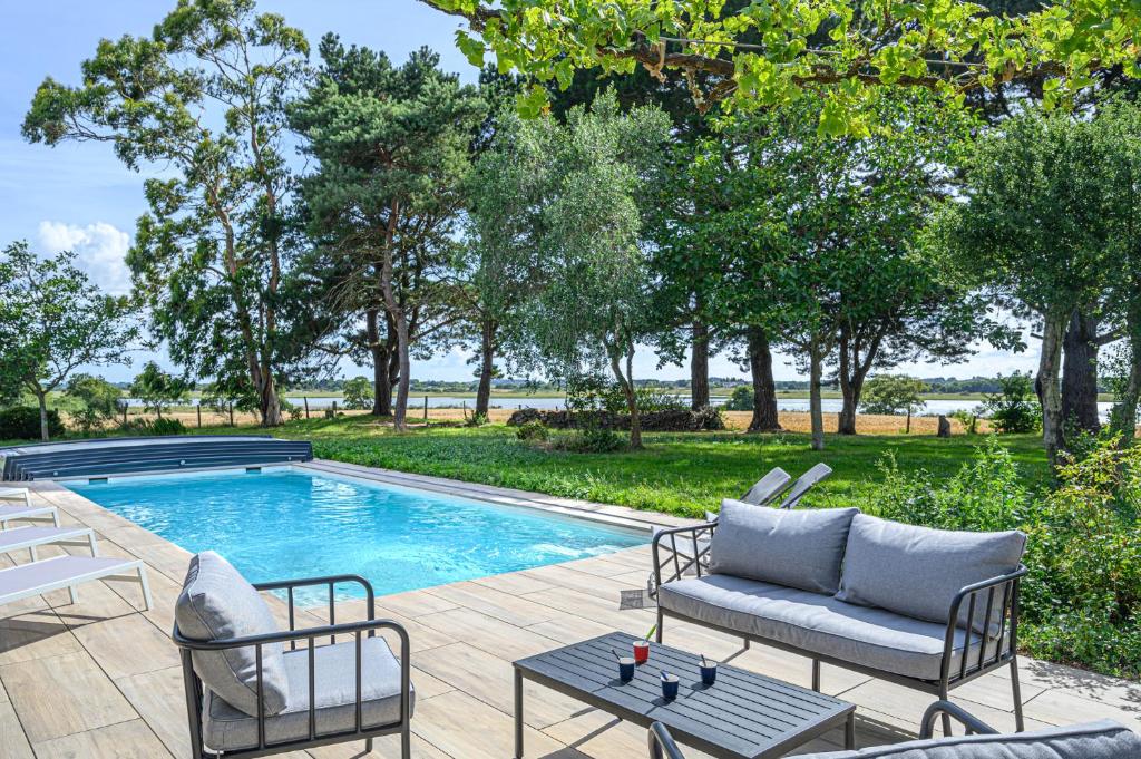 a swimming pool with two chairs and a couch next to at VILLA CALYPSO - Longère avec piscine vue mer in Noyalo