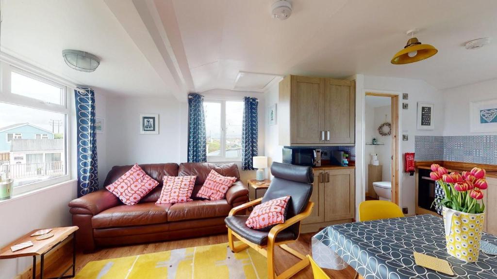 a living room with a brown leather couch and a bed at E08 Boness E8, Riviere Towans in Hayle