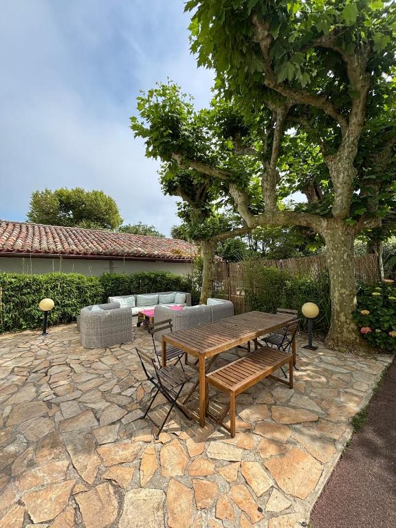 a wooden table and bench on a stone patio with a tree at Maison au coeur de Guéthary in Guéthary