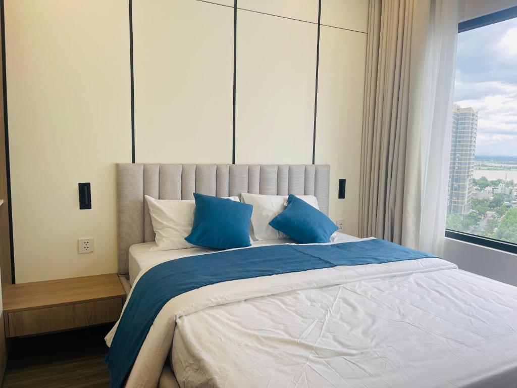 a bedroom with a bed with blue pillows and a window at Đô thị Vinhomes Grand Park in Gò Công