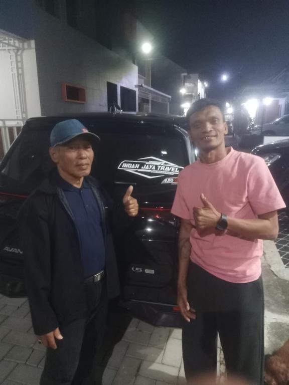 two men are standing in front of a car at Indah Jaya Travel in Kedungmangu