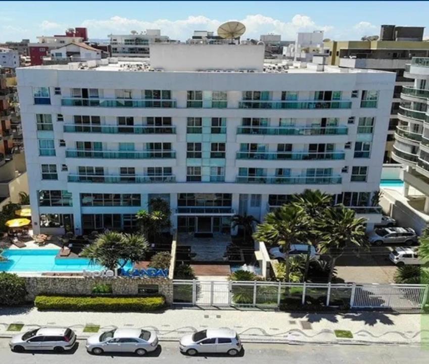 a large white building with cars parked in a parking lot at Mandai Apart - Beira Mar in Cabo Frio