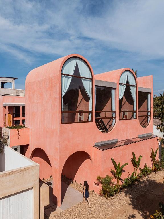 a woman walks past a pink house with large windows at Amplitude Coliving in Brisas de Zicatela