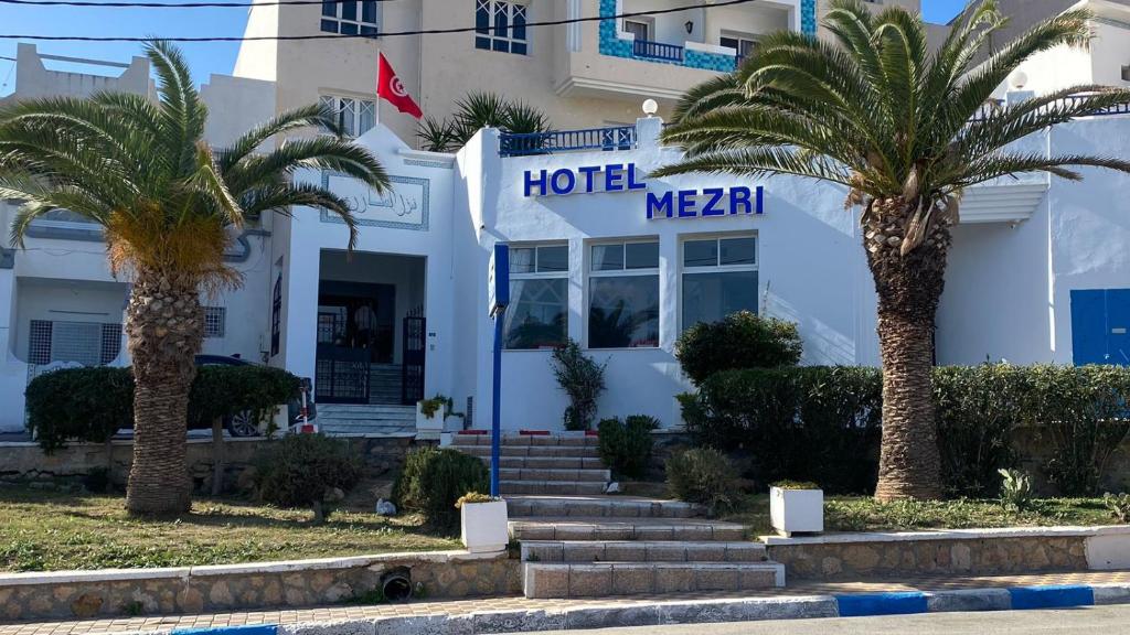 a hotel with palm trees in front of a building at Hotel Mezri in Monastir