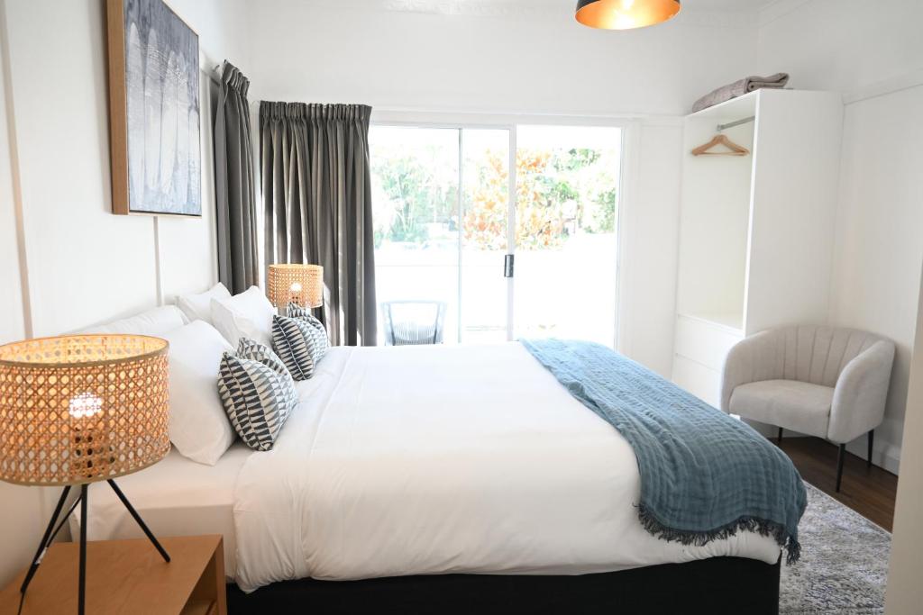 a white bedroom with a large bed and a chair at Soluna House in Byron Bay