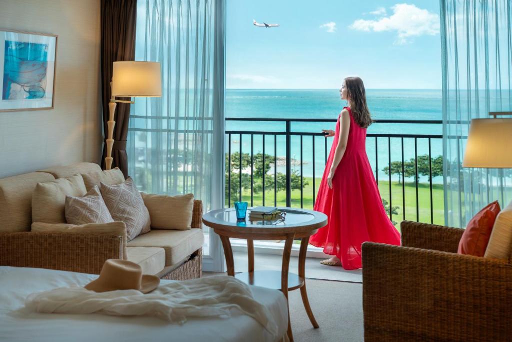 a woman in a red dress looking out the window of a hotel room at Southern Beach Hotel & Resort Okinawa in Itoman