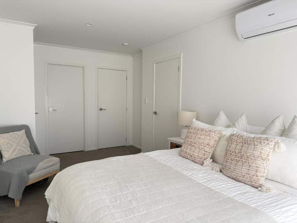 a white bedroom with a white bed and a chair at Sarah's Guest House in Havelock North