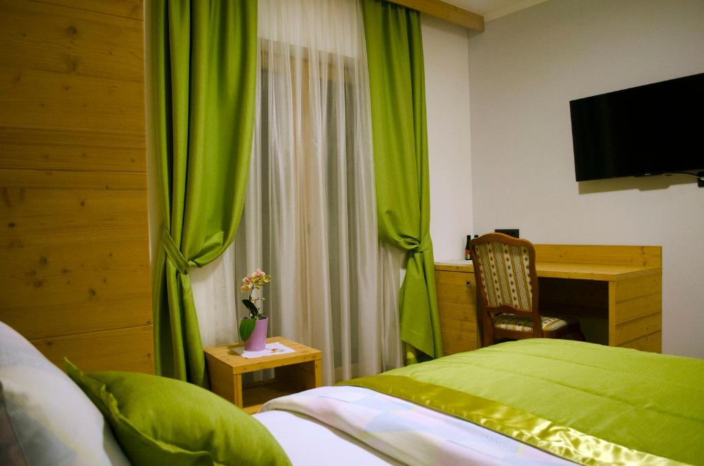 1 dormitorio con cortinas verdes, escritorio y cama en Guest House Gostišče Jutriša, en Rogatec