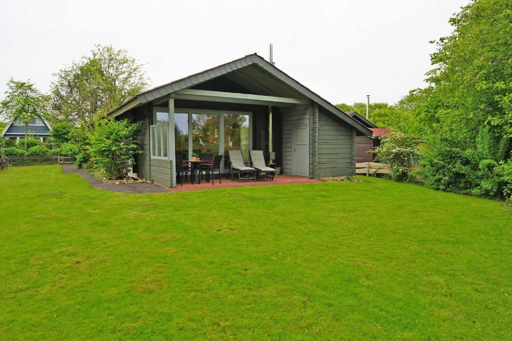 a small green house with a patio and green grass at Blockhaus mit grosser überdachter Terrasse in Damp