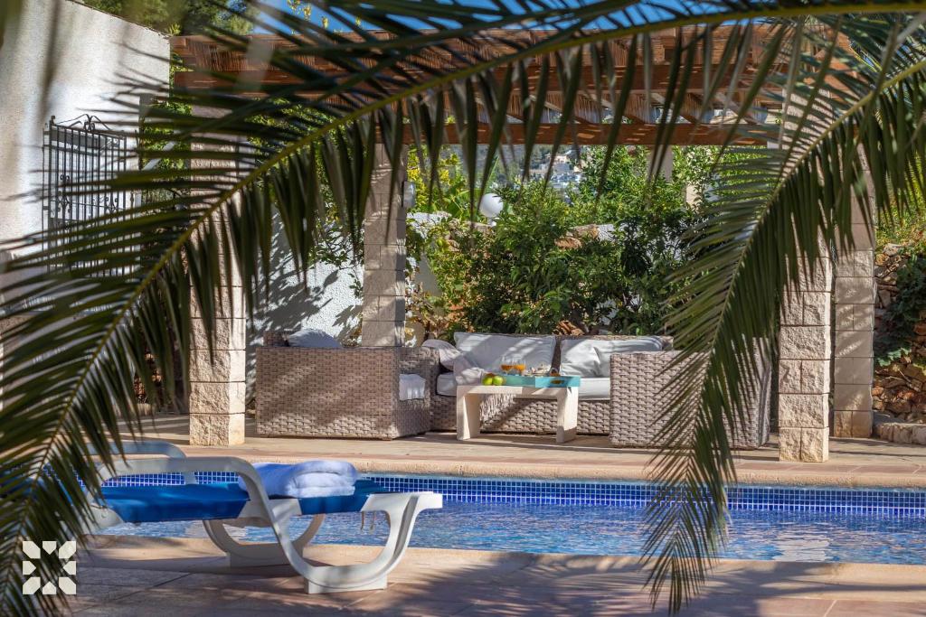a swimming pool with chairs and a table and a palm tree at Villa Ananas by Abahana Villas in Moraira