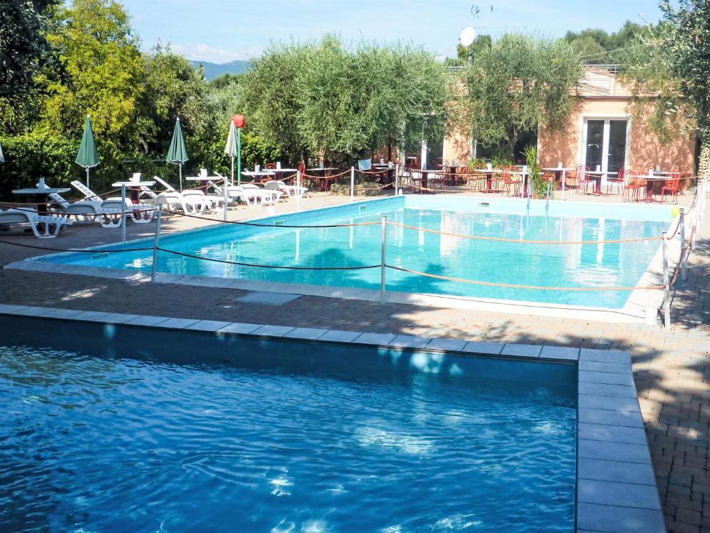 a swimming pool with blue water and tables and chairs at Apartment Borgoverde-5 by Interhome in Imperia