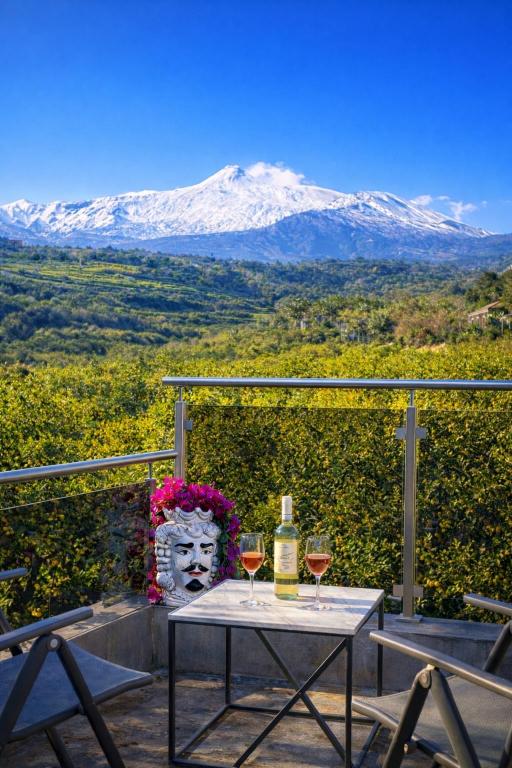 a table with two glasses of wine and a snow covered mountain at Limoneto Etna View in Giarre
