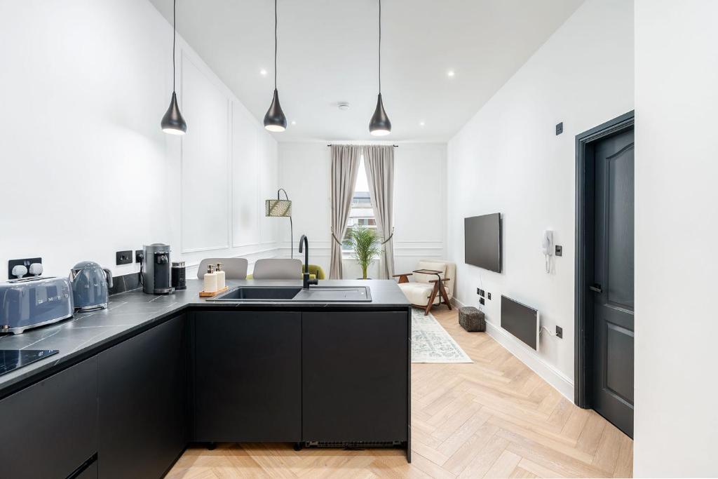 a kitchen with black cabinets and a living room at Luxury High-Ceiling Apartment Central Altrincham in Altrincham