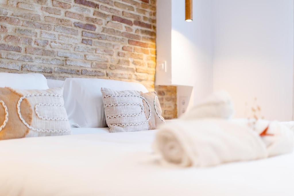 a white bed with pillows and a brick wall at Pickman Suites in Seville