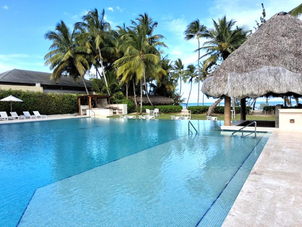 a swimming pool with a straw umbrella and palm trees at Beachfront Portillo Residence in Las Terrenas