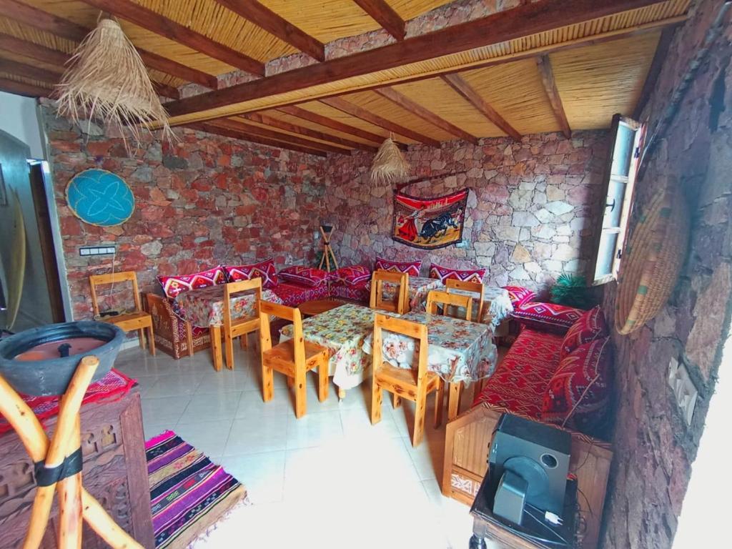 a room with a table and chairs and a stone wall at AZULI ⵣ Hostel Mirleft in Mirleft