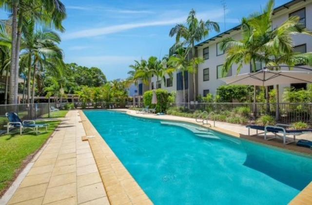 a swimming pool in front of a building with palm trees at Rainbow Beach Resort overlooking Pool in Rainbow Beach