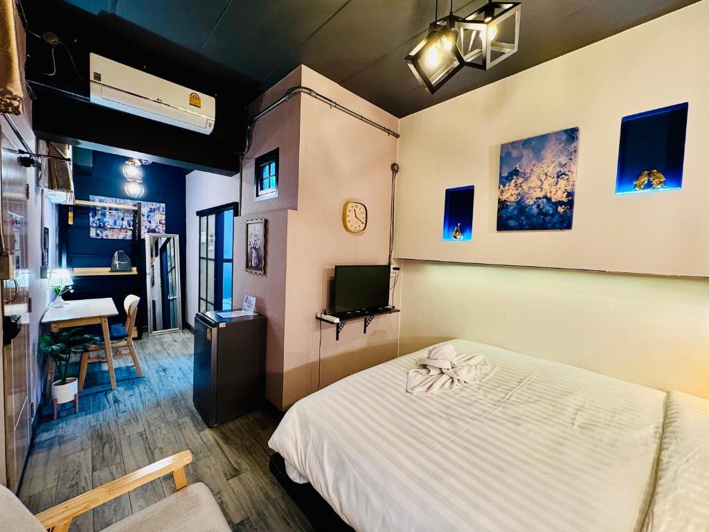 A compact bedroom with a television, air conditioner, refrigerator and adjoining desk area.