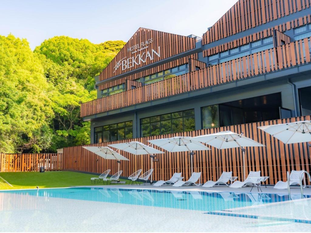 a building with chairs and umbrellas next to a pool at Hotel Flags Sasebo KujuKusima in Sasebo