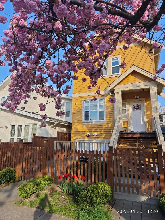 a yellow house with a fence and a flowering tree at Modern 2BR Suite Steps to SkyTrain in Vancouver