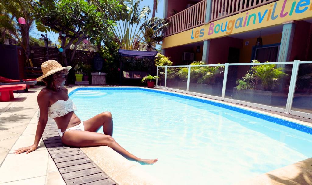 a woman in a bikini sitting next to a swimming pool at Hôtel les Bougainvilliers in Saint-Gilles-les-Bains