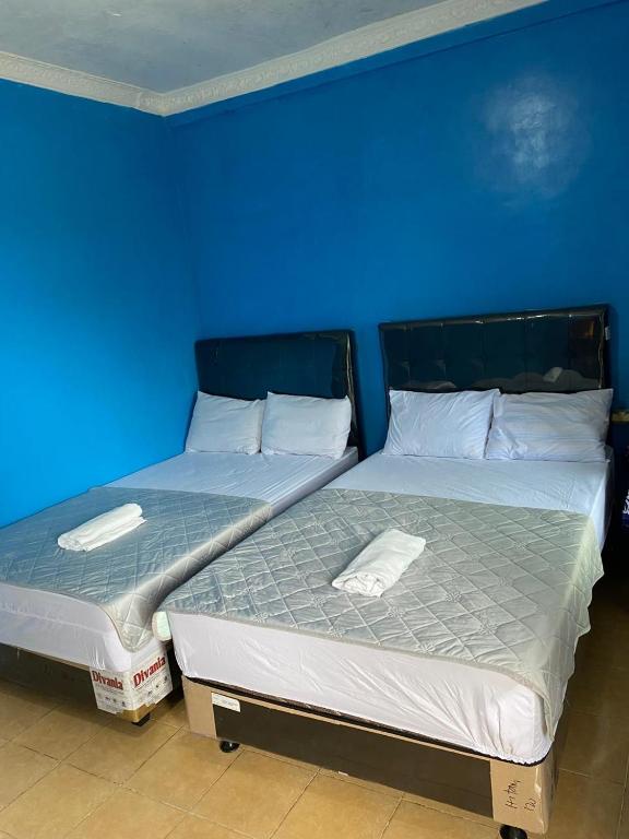 two beds in a room with a blue wall at Hotel Carollina Syariah in Girijati