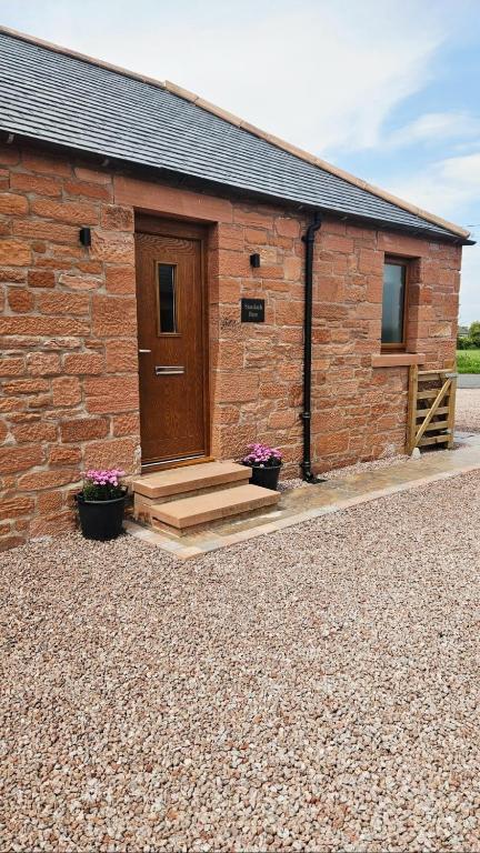 a brick building with a wooden door and stairs at Cosy wee cottage -modern, open plan, parking, EV in Glencaple