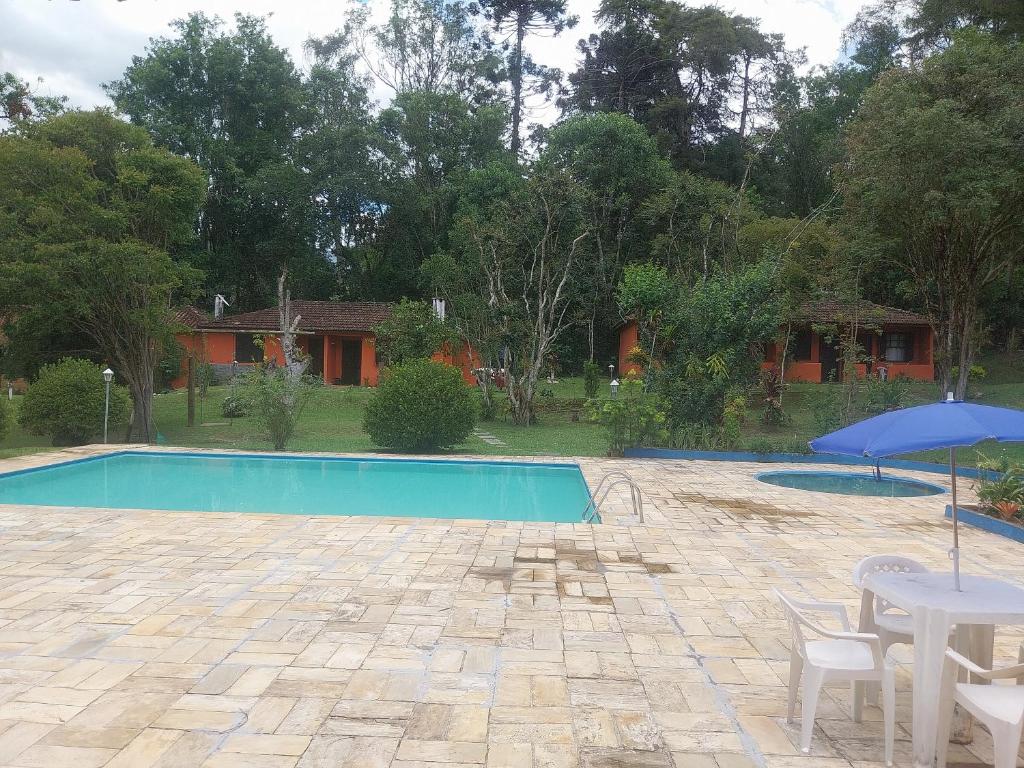 a swimming pool with a table and an umbrella at Chalé Refúgio na Alameda Maringá MG in Bocaina de Minas