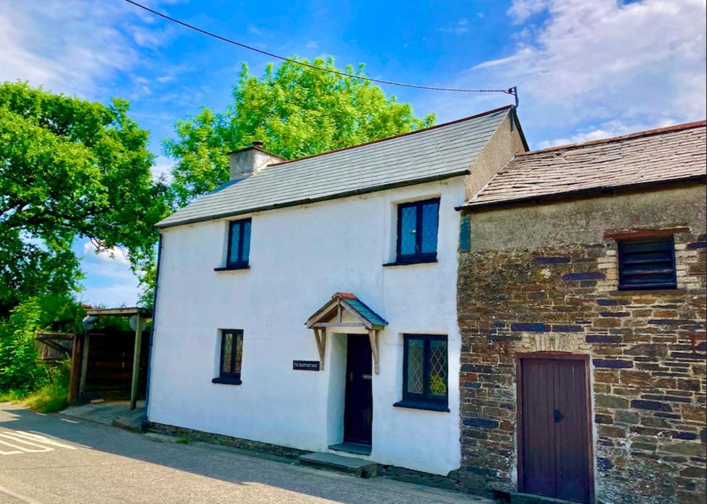 an old white house with blue windows on a street at The Eliot Cottage in South Petherwin
