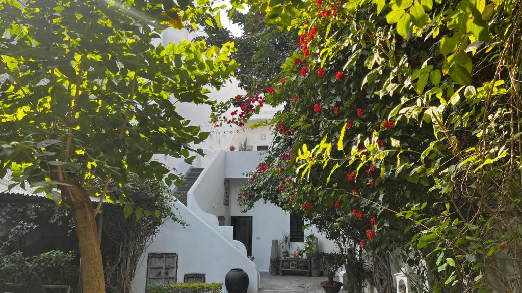 a white building with red flowers and trees at Mosaics Guest House in Jaipur